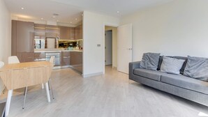 Un salon moderne avec un canapé gris, une table à manger en bois et une cuisine en arrière-plan.