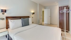 Une chambre d’hôtel comprenant un lit, une table de chevet, une lampe fixée au mur et un porte-manteau.