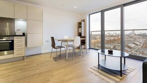A modern kitchen with a built-in oven and a dining area with a round table and chairs. - Modern 1 Bedroom Apartment Near Canary Wharf With Balcony (London)