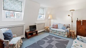 En hyggelig stue med en sofa, et fjernsyn, en lampe og en radiator.