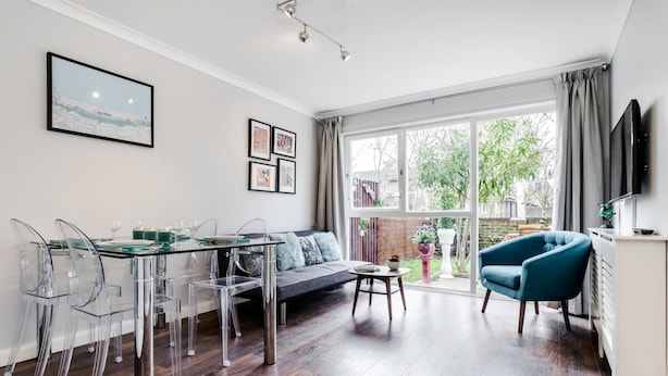 A modern living room with a glass dining table, clear chairs, a sofa, and a blue armchair. - Lovely 2 Bedroom Apartment With Garden, South Bank Westminster (London)