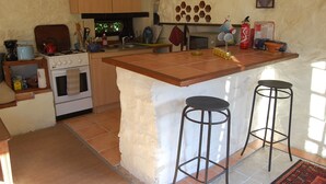 A kitchen with a central island, two bar stools, a stove, a microwave, and various kitchen items. - Peaceful Detached Cottage Studio French Countryside Private Garden Nature Lovers (champagne mouton)