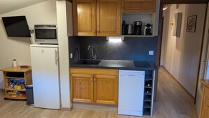 A compact kitchen with wooden cabinets, a built-in microwave, a dishwasher, and a sink. - Apartment Combloux sleeps 4 at the foot of the slopes (Combloux)
