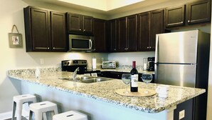 Una cocina con armarios oscuros, un refrigerador de acero inoxidable, encimera de granito y taburetes de bar blancos.