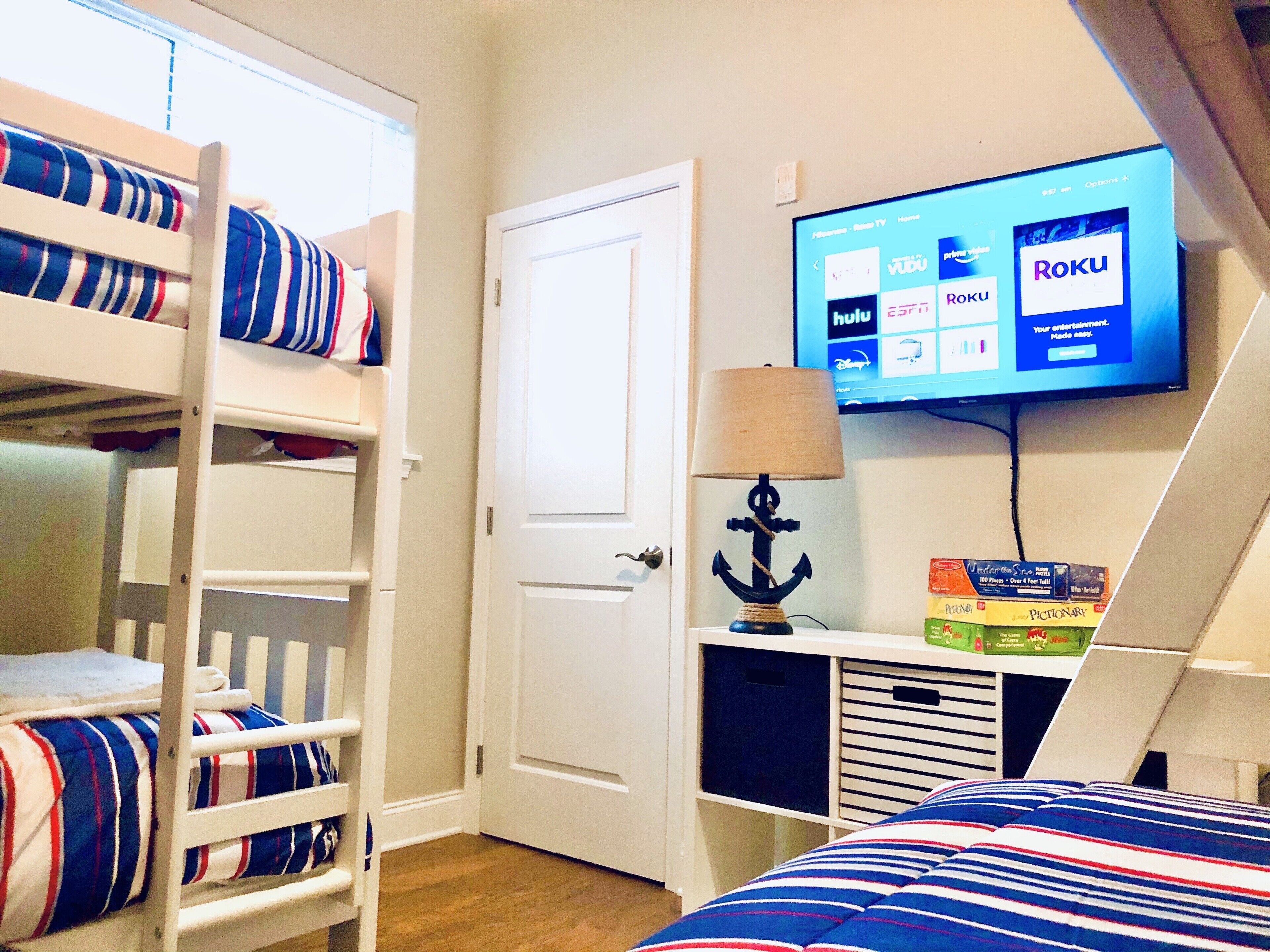 A room with bunk beds, a television displaying Roku, and a lamp.