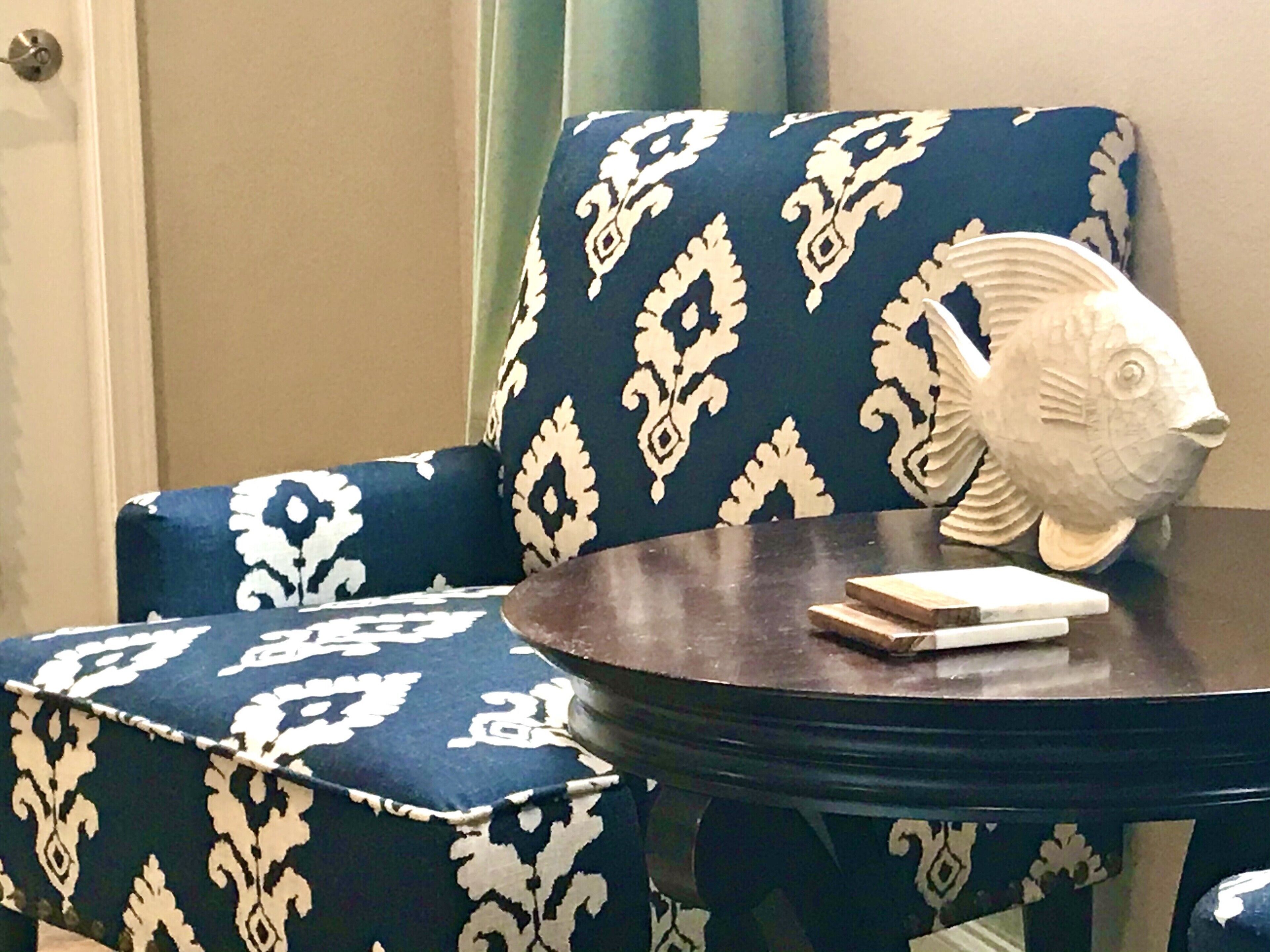 A chair with a dark blue and white patterned upholstery, a round wooden table, and a white fish-shaped object on the table.