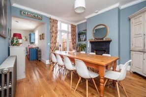 Een eethoek met een houten tafel en witte stoelen, een open haard, en een bord met de tekst 'CIRCUS' aan de muur.