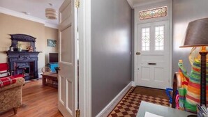 Ein Zimmer mit Schachbrettfußboden, Kamin, Sofa und einer Tür mit Buntglasverzierungen.