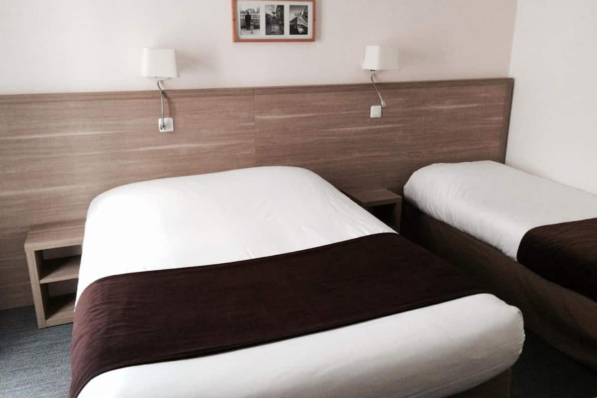Habitación de hotel con dos camas, cabecera de madera, lámparas de noche y una fotografía en el marco en la pared.