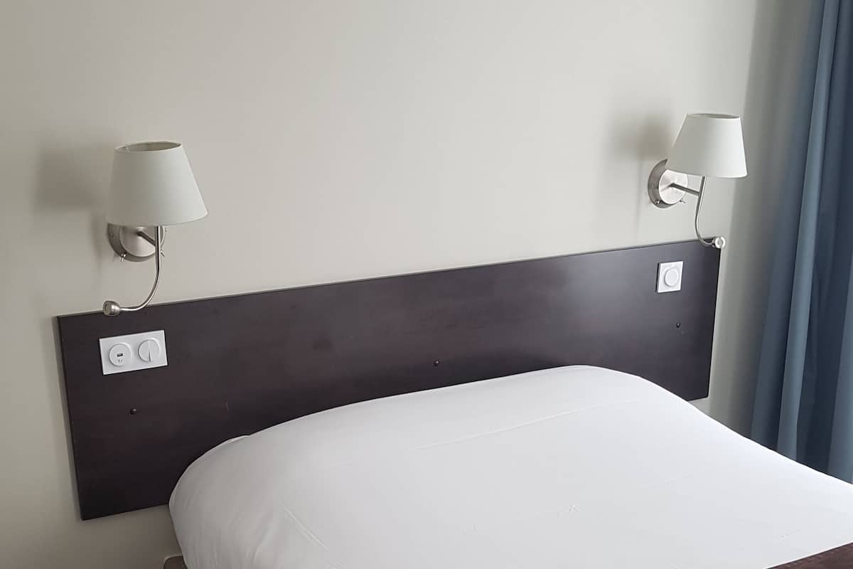Habitación de hotel con una cama grande, dos lámparas de noche, una mesita auxiliar pequeña y un enchufe.