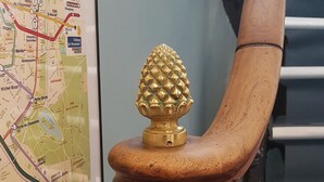 A wooden chair with a decorative pineapple ornament, positioned next to a wall-mounted map. - Hotel Cosmos (Paris)