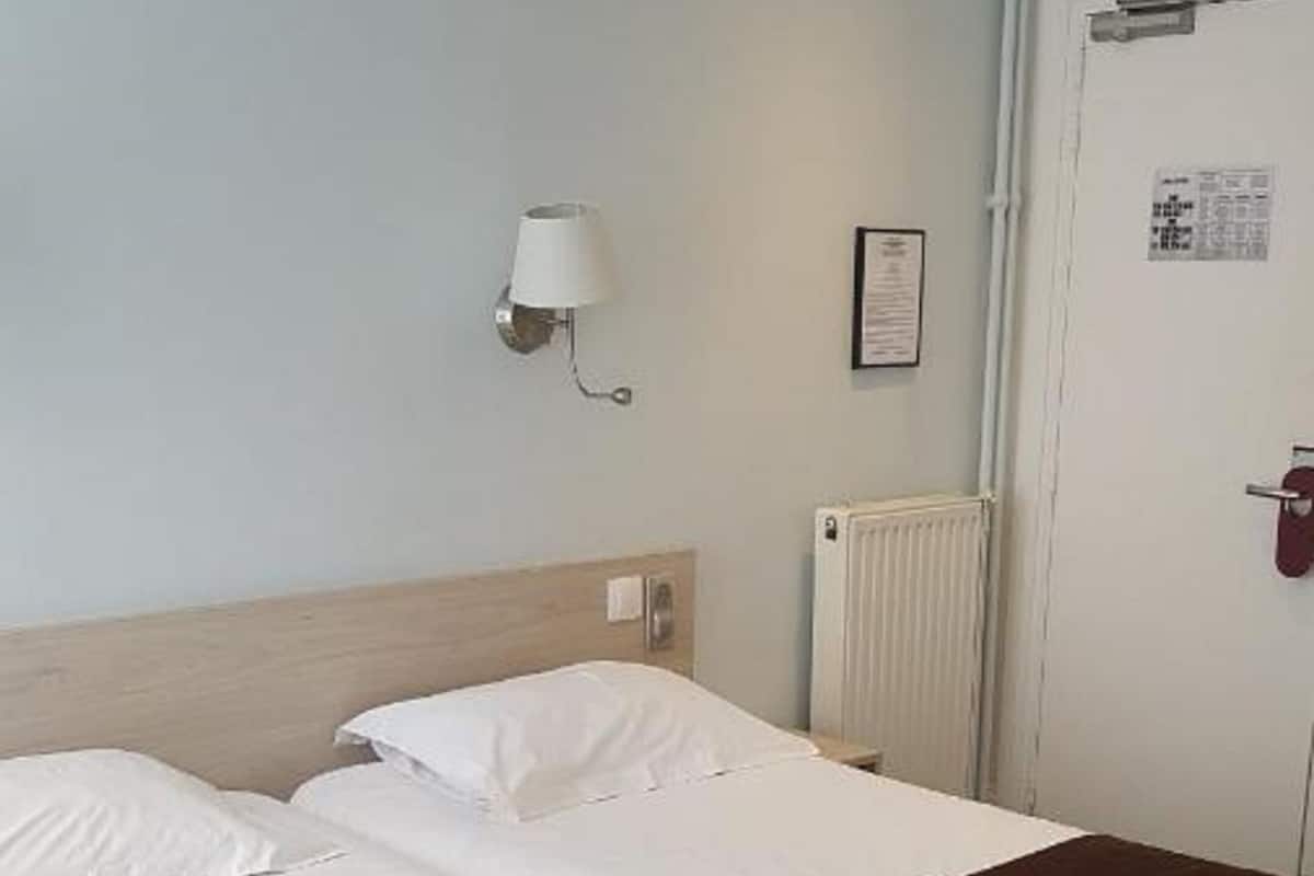 Una habitación de hotel con cama doble, lámpara de noche, radiador y puerta con cerradura.