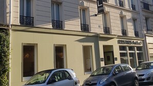 A multi-story hotel with balconies, a sign indicating it is a hotel, and parked cars in front. - Hotel Cosmos (Paris)