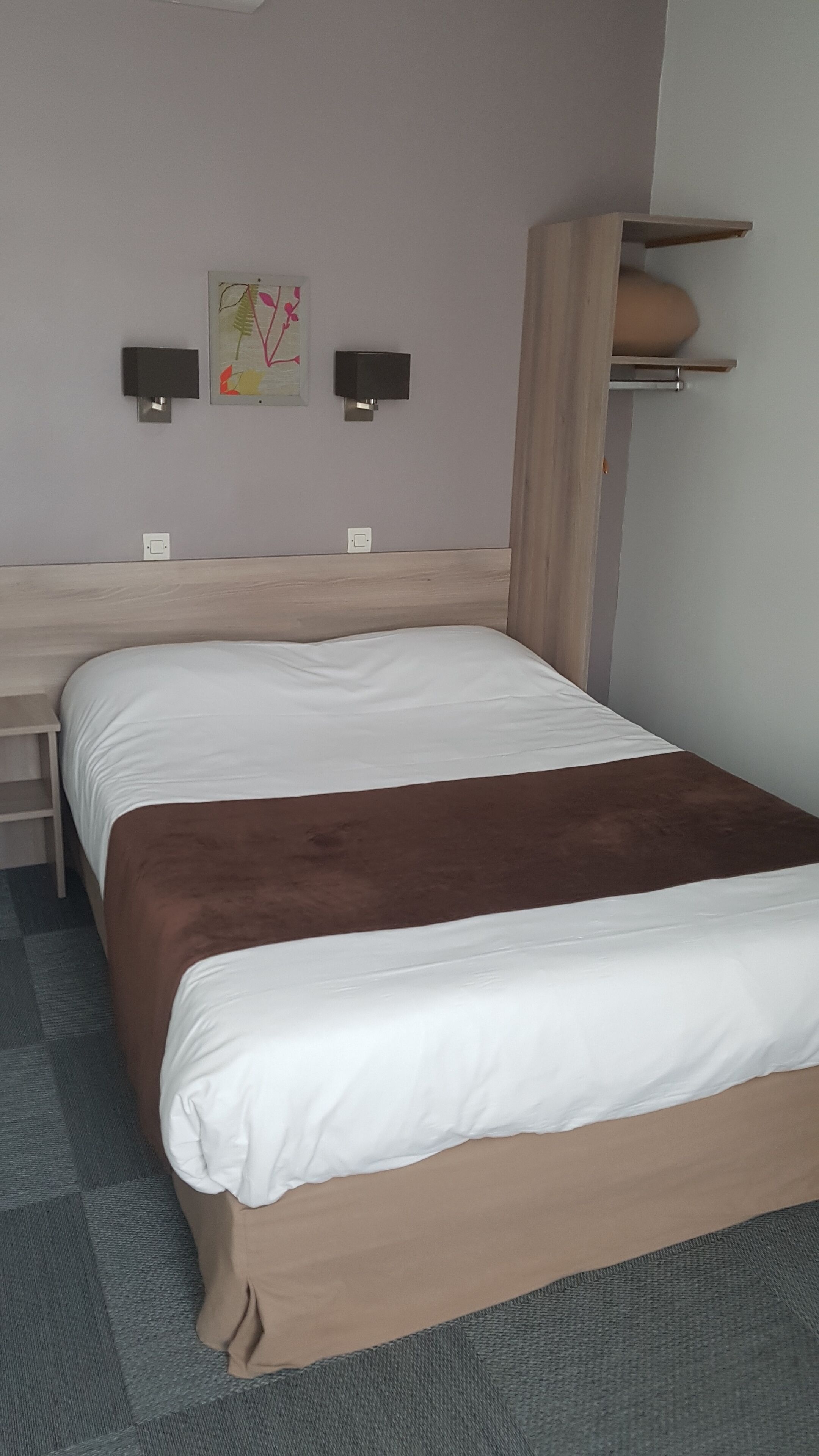 Quarto com cama, escrivaninha e duas luminárias de parede.
