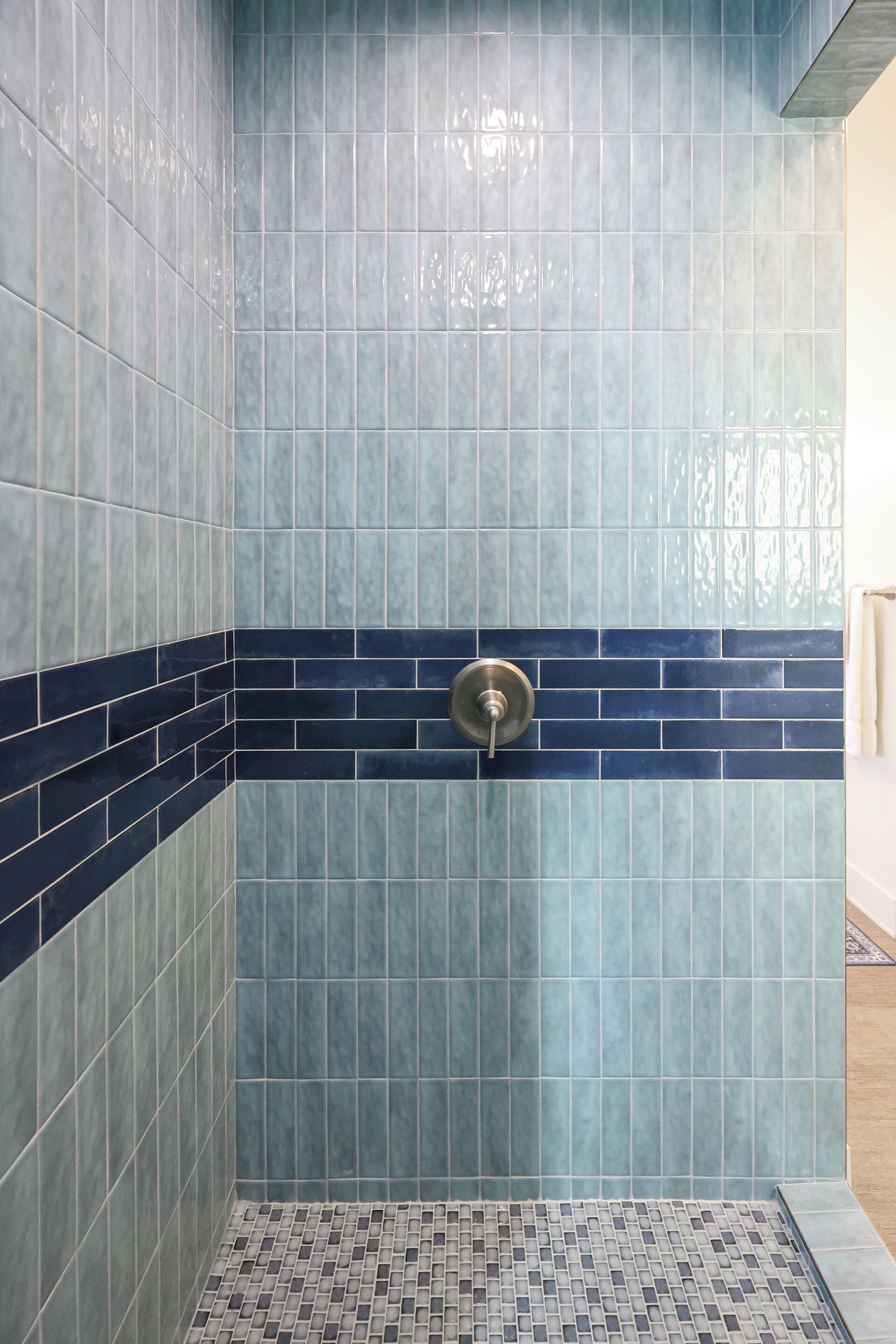 Un baño con azulejos azules y azul oscuro, una zona de ducha y piso de cerámica.