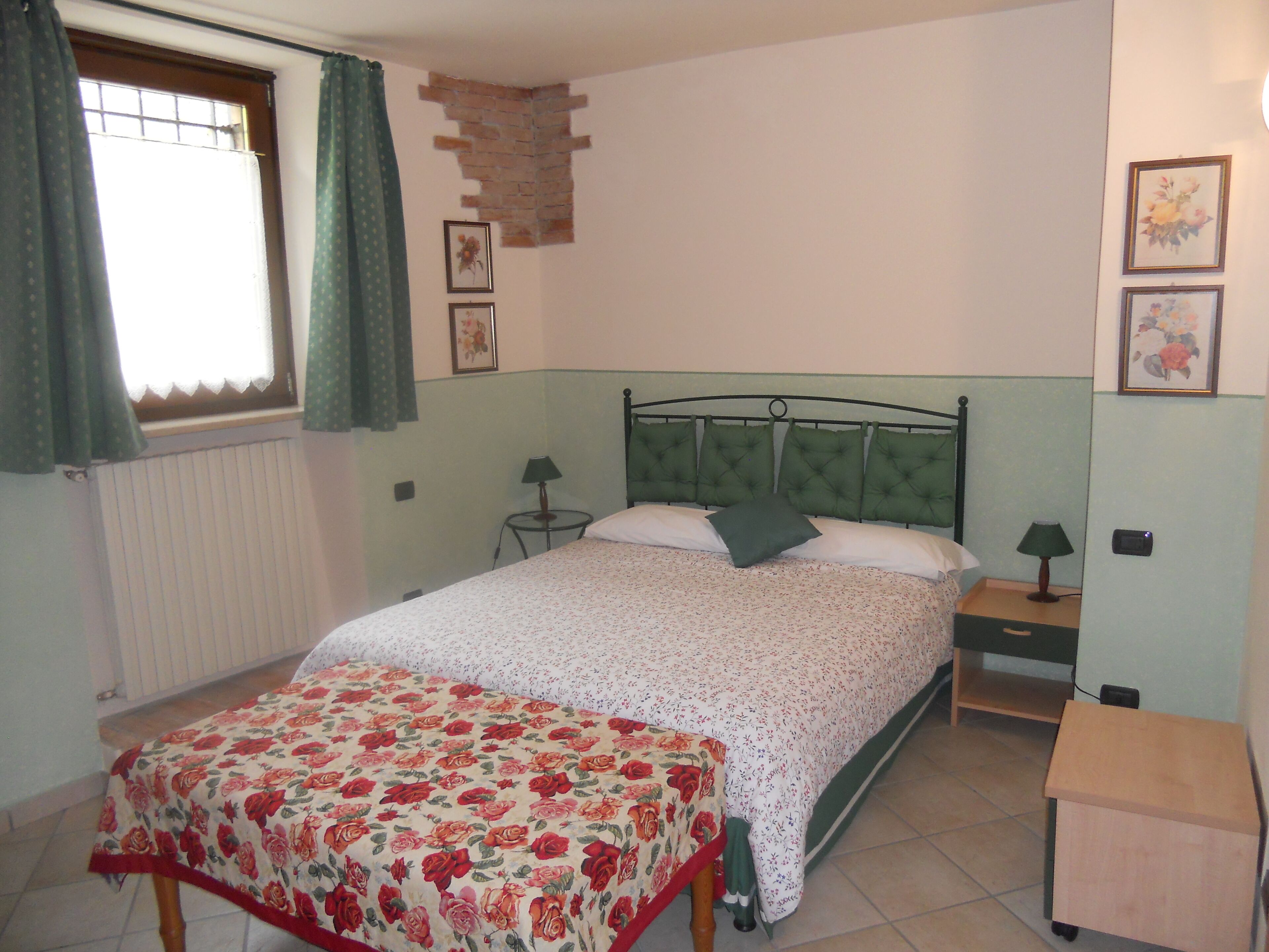 Un dormitorio con cama, mesita de noche, lámpara, radiador y ventana con cortinas.
