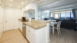 A modern kitchen with white cabinetry, granite countertops, and a dining area with a table and chairs.