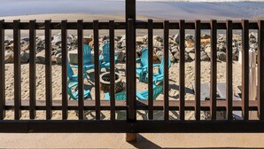 A beach view from a covered area with a wooden fence, blue chairs, and a table.