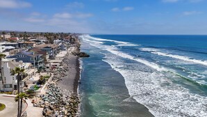 Zona residencial costera con casas a lo largo de la playa, costa rocosa y olas azules claras.