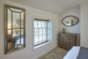 A bedroom with a large mirror, a dresser, a window with blinds, and a bed. - Host & Stay | Dunsley Chapel (Whitby)