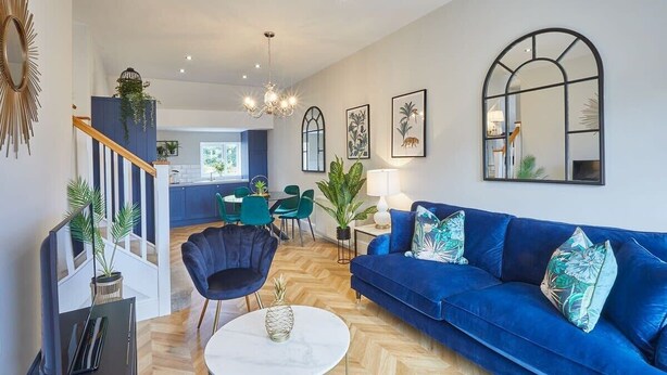 A modern living room with a blue sofa, a round coffee table, and a staircase leading to a kitchen. - Host & Stay | The Penthouse at Prospect Hill Apartments (Whitby)