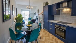 A modern kitchen with blue cabinets, a built-in oven, and a dining area with teal chairs and a glass table. - Host & Stay | The Penthouse at Prospect Hill Apartments (Whitby)