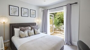 A bedroom with a large bed, a bedside table, a lamp, and a view of an outdoor patio.