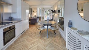 A modern kitchen with white cabinetry, a round dining table with chairs, and a herringbone wood floor.