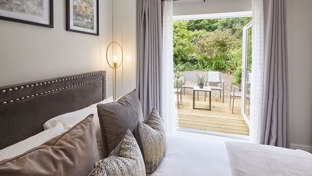 A bedroom with a large bed, a bedside table, and a view of an outdoor patio with a table and chairs.