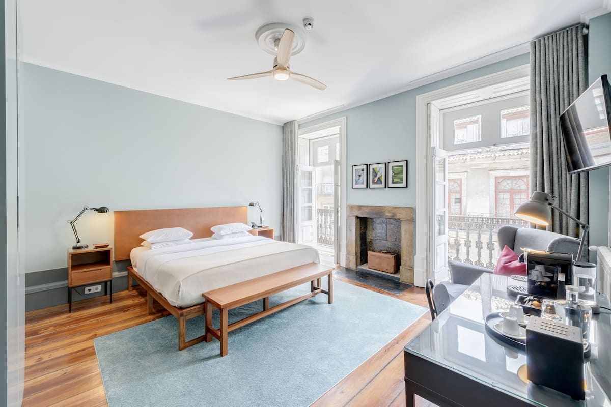 Una habitación de hotel moderna con una cama grande, un escritorio con silla, una chimenea y un balcón con vistas a la ciudad.