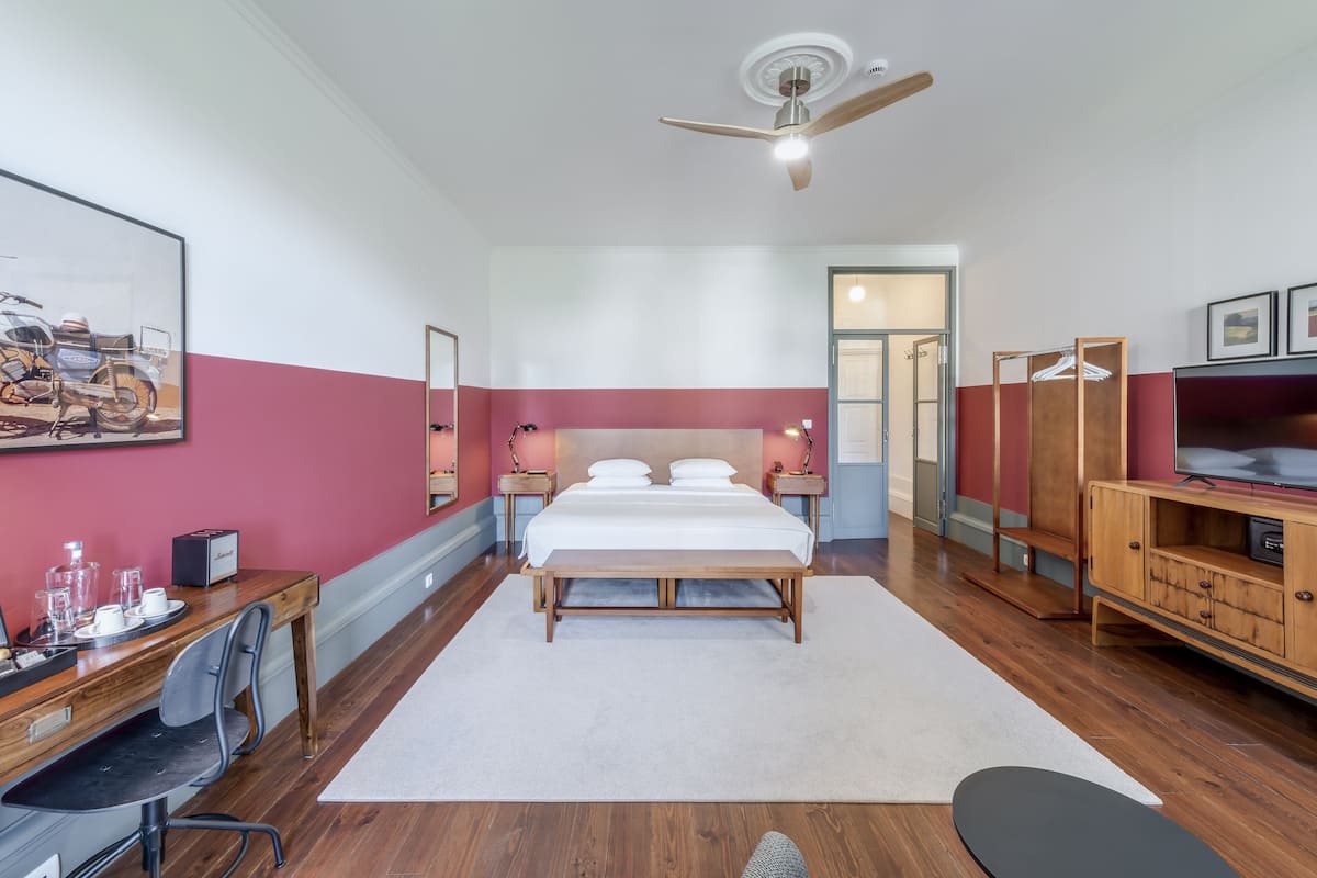 Una habitación de hotel moderna con una cama grande, muebles de madera, un ventilador de techo y un televisor.