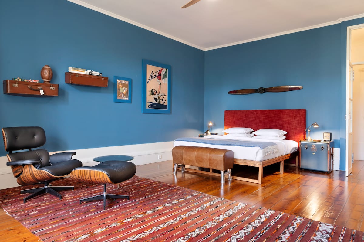 Un dormitorio con cama, cabecera roja, suelo de madera, pared azul y ventilador de techo.