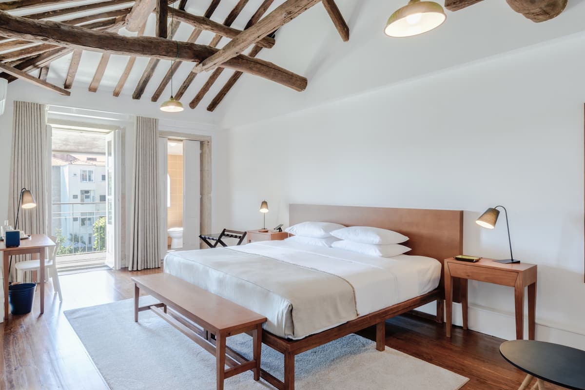 Un dormitorio con cama de madera, mesitas de noche, un banco y vistas al exterior.