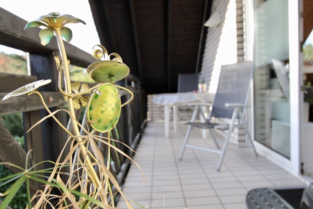 Un balcón con mesa y sillas, barandilla de madera y plantas en macetas.