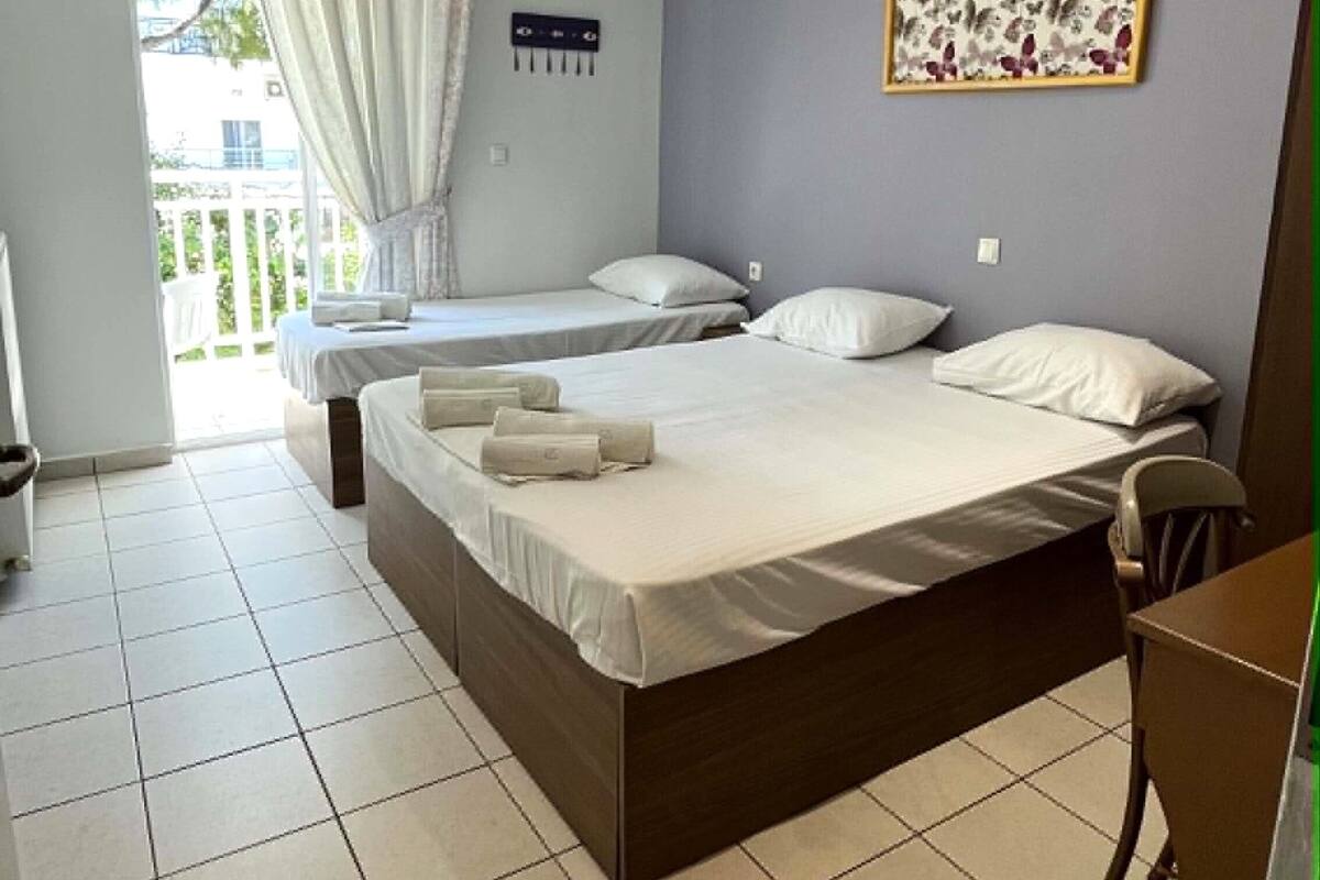 A bedroom with two beds, a window with curtains, a wall-mounted air conditioner, and a framed picture.