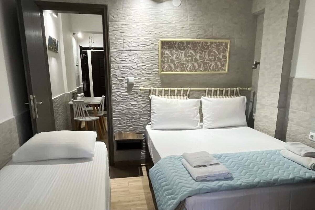 A hotel room with two beds, a small table, a mirror, and a wall-mounted light fixture.