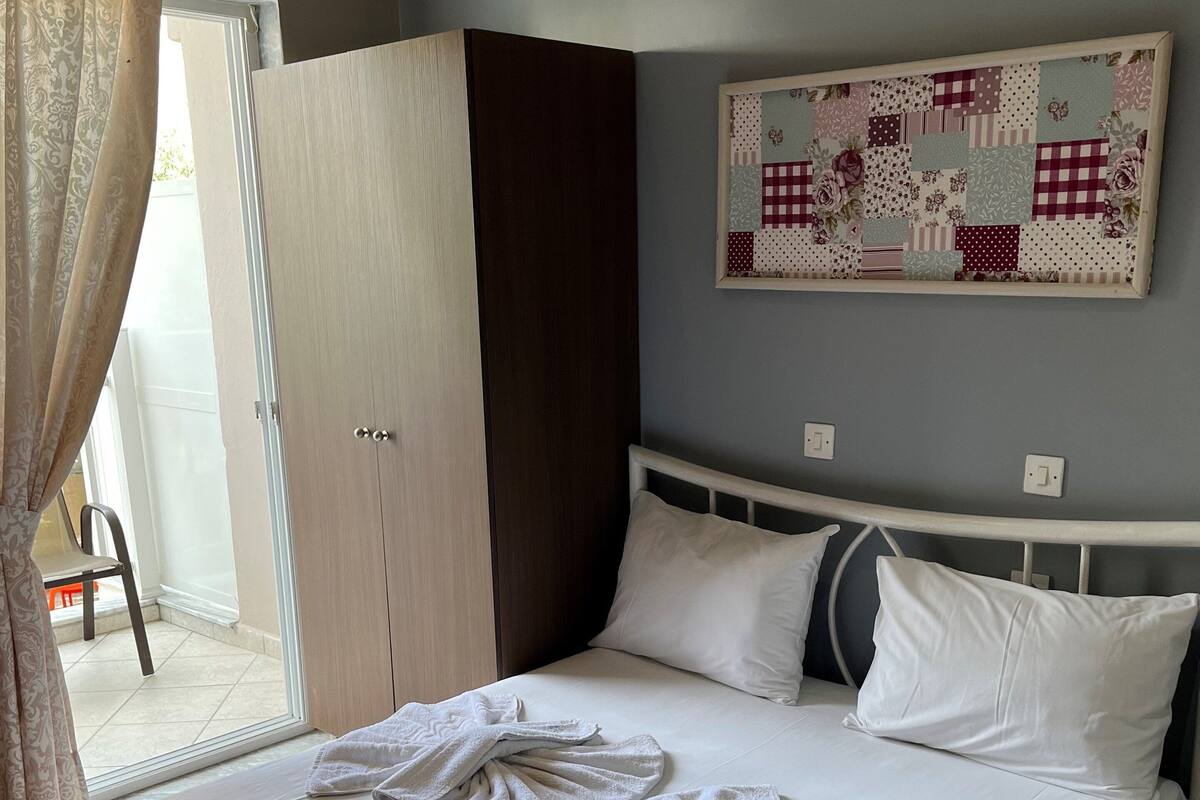A bedroom with a bed, a wardrobe, a painting on the wall, and a view through an open door.