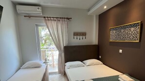 A hotel room with two single beds, a large window with curtains, a wall-mounted air conditioner, and a patterned artwork. - Grecian Sea (Thasos)