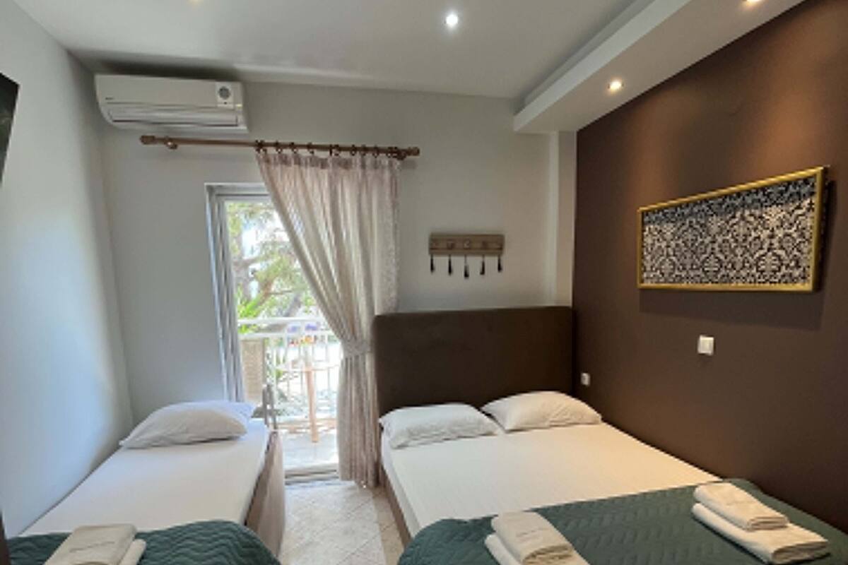 A hotel room with two single beds, a large window with curtains, a wall-mounted air conditioner, and a patterned artwork.