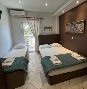 Habitación de hotel con dos camas individuales, un ventanal con cortinas, aire acondicionado de pared y una obra de arte con motivos decorativos.