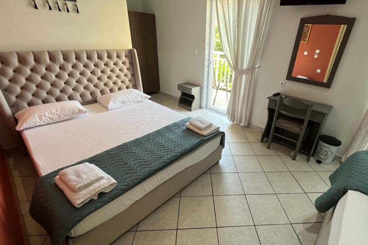 A hotel room with a large bed, a small bedside table, a chair, a TV mounted on the wall, and a window with curtains.
