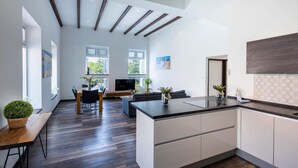 Una cocina moderna con una isla central, suelo de madera y una zona de comedor con televisor y asientos.