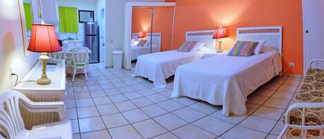 A hotel room with two beds, a desk with a lamp, a chair, and a small table.