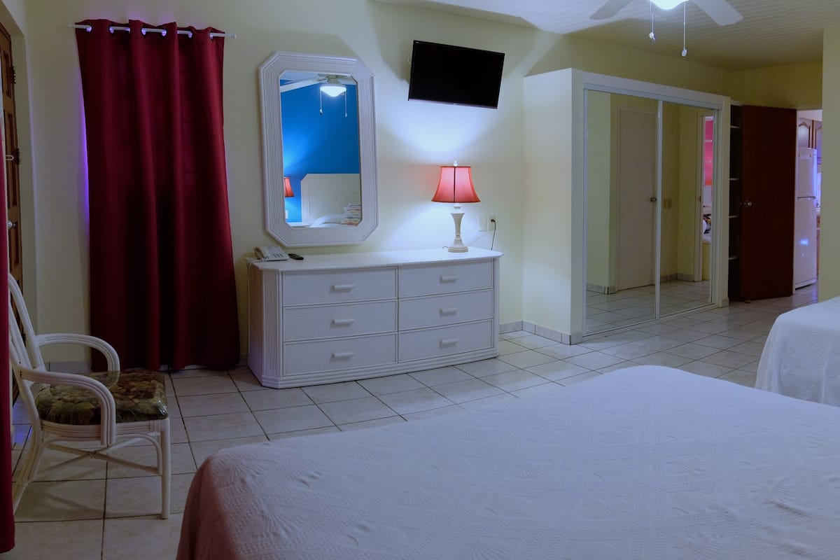 A hotel room with two beds, a wardrobe, a mirror, a desk with a lamp, and a painting on the wall.