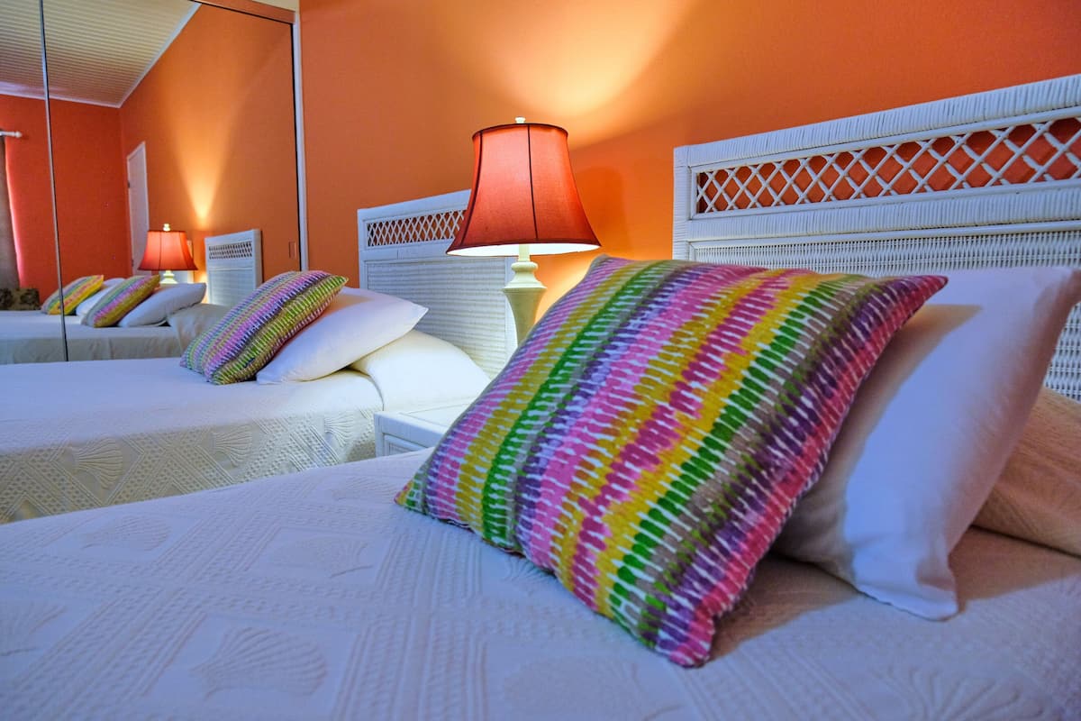 A hotel room with two beds, each with a white headboard and a colorful striped pillow.
