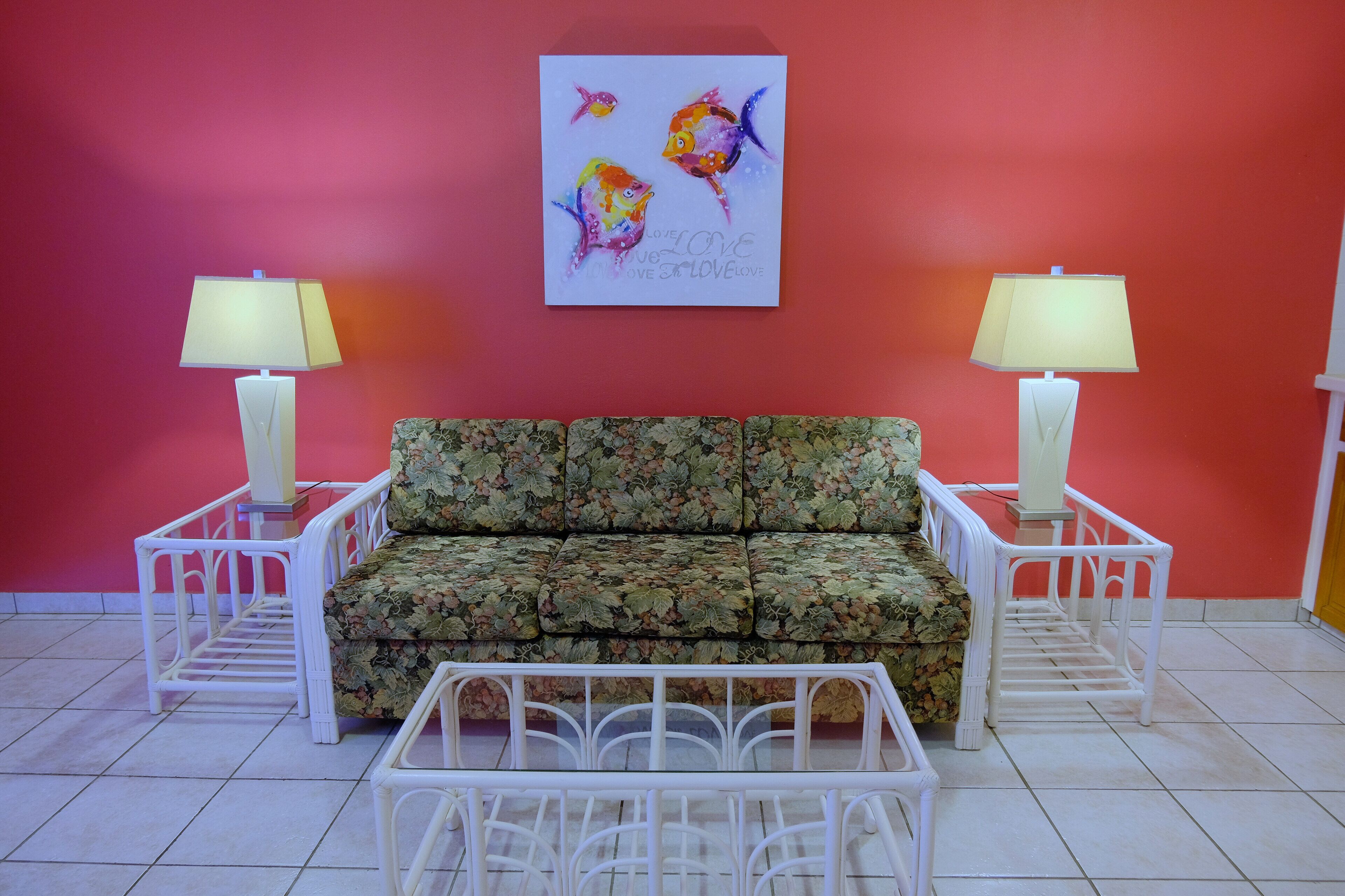 A room with a floral sofa, two white nightstands with lamps, and a colorful artwork on the wall.