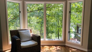 Habitación de esquina con una silla de mimbre, ventanas amplias y piso de madera.