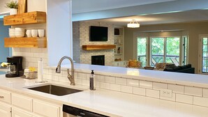 Una cocina moderna con muebles blancos, lavavajillas de acero inoxidable y cafetera negra.