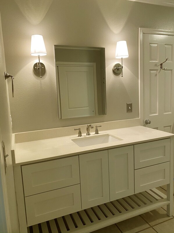 A bathroom with a double sink, two wall-mounted lights, a large mirror, and a door with a handle.