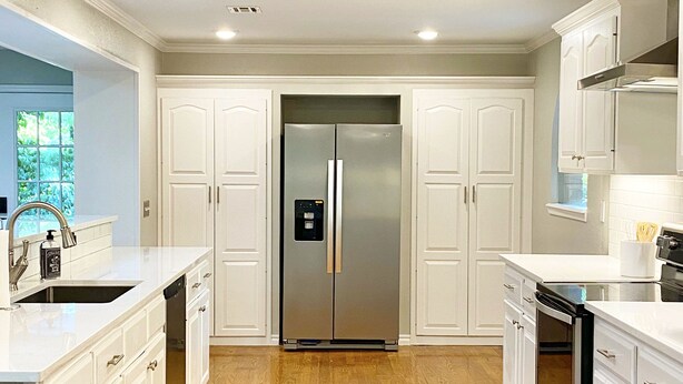 Una cocina moderna con armarios blancos, un refrigerador de acero inoxidable y piso de madera.